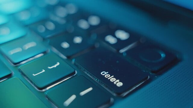 Close up on finger presses on Delete key on laptop keyboard in dark office room. Man or hacker programmer deleting information or item removing and erasing it from system. Undoing hiding private data