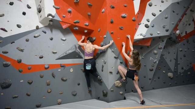 Two climbers working on indoor wall problems in bouldering center, showing strength and technique during training. Authentic video for active recreation, endurance, focus, and healthy lifestyle use