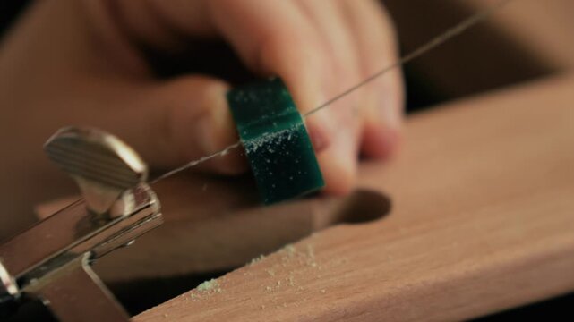 Close up macro view of a jeweler shaping a green wax ring model using a fine saw on a wooden bench peg.