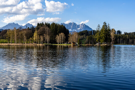 spring Tyrolean lake Schwarzsee with reflection of blue sky and white clouds, in the background the Wilder Kaiser Alpine massif with remnants of snow