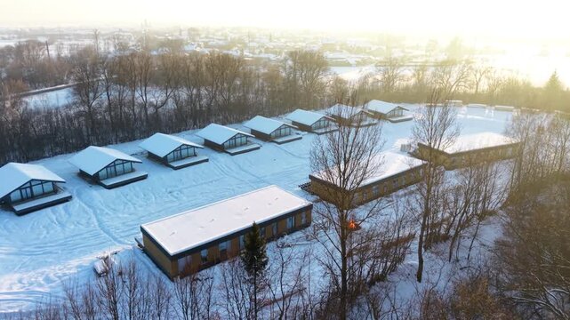 Aerial view of wooden frame houses under construction covered in snow at sunset, showcasing winter building process, rural development and modern eco housing project