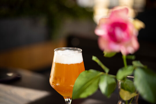 Golden craft beer served in an elegant tulip glass with a creamy foam head at an outdoor caf&eacute;. A softly blurred pink rose and natural bokeh create a relaxed summer atmosphere with selective focus.