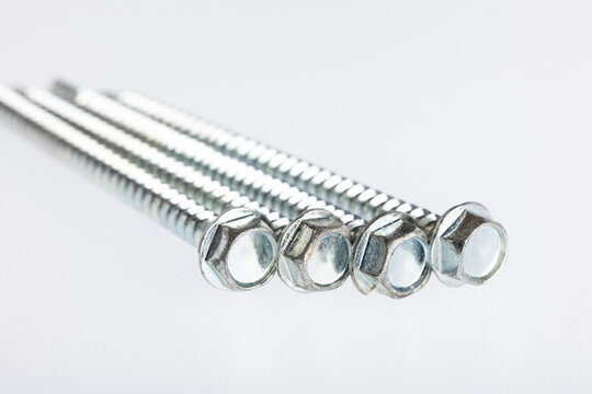 Close-up of metal hex bolts. The bolts are shiny and have a threaded stem, located on a white background.