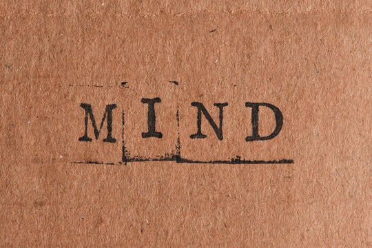 Word MIND stamped with black ink on textured brown cardboard paper background, centered composition.