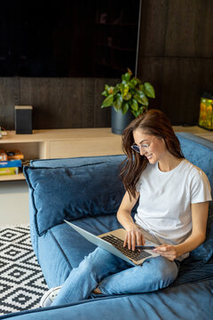 Smiling young woman with laptop in hands sitting on a sofa