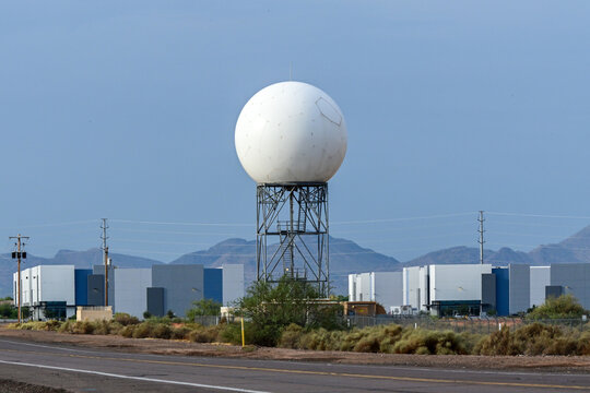 Weather radar radome on a steel tower overlooking an industrial area, representing meteorological monitoring, aviation weather systems, and atmospheric observation infrastructure