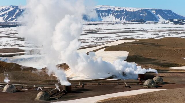 Steam emanates from volcanic site. Vast geothermal installation amid volcanic and mountain scenery