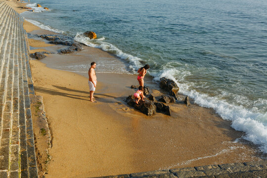 Father and Two Daughters Exploring Rocks on a Sandy Beach by the Sea