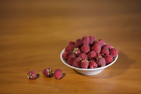 Ripe organic red raspberries in a white bowl on a wooden table with copy space.