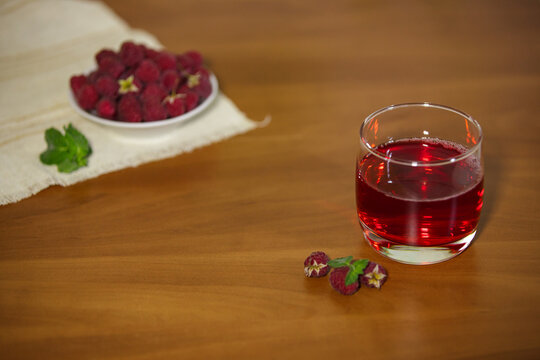 Glass of red raspberry juice on a wooden table with fresh berries and copy space.