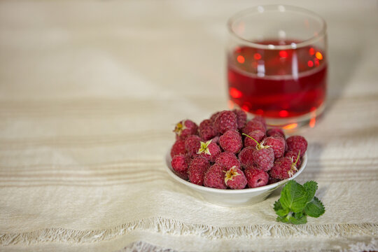 Fresh ripe raspberries in a bowl with juice and mint on a linen tablecloth.