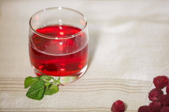 Glass of red raspberry juice with mint on a linen tablecloth with copy space.
