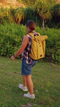 Vertical video. Female Traveler Walking Across Coastal Grassland on Nusa Penida Near Rugged Ocean Cliffs, Exploring Remote Island Landscape During Golden Sunset