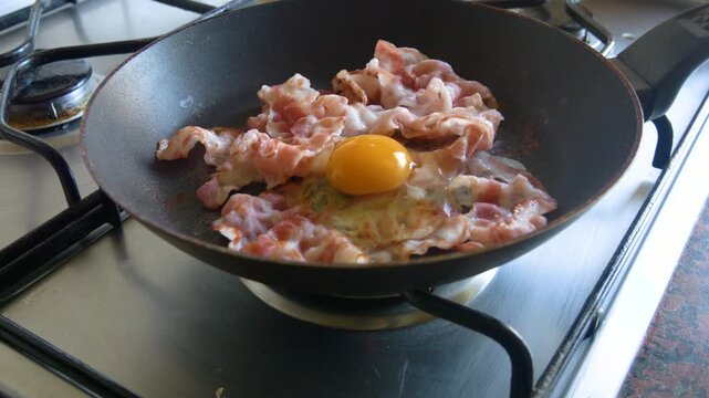 Frying eggs with bacon in pan for homemade breakfast