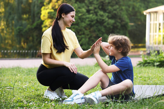 Morning exercise. Mother giving high five to her son in park