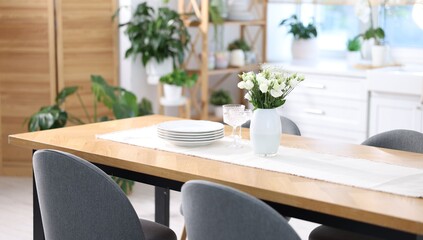 Fototapeta premium Stylish setting with vase of flowers, plates and glasses on wooden table in kitchen