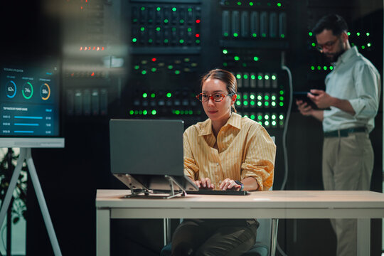 It engineer woman working on laptop in modern data center, managing server operations and cloud computing infrastructure