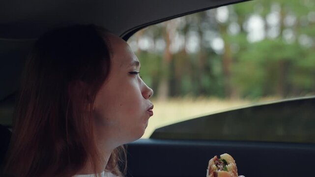 woman girl eating burger car, happy person, Taking a burger bite, Concentrated eating scene, Outdoor snack session, Fast food happiness, Simple pleasures on road, Girl s favorite snack, Quiet meal in