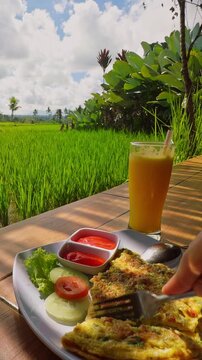 Vertical video. First Person Breakfast at Open Air Cafe Overlooking Green Rice Fields, Fresh Tropical Meal And Juice Served Beside Scenic Agricultural Landscape