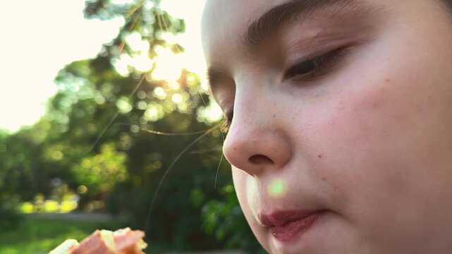 Close up of eating, park day, focused child, natural backlight, sandwich in hand, fun experience, sunlight rings, striped top, peaceful vibe, greenery view, Hungry in park, outdoor lunch, joyful child