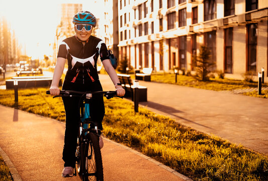 Smiling female cyclist riding bicycle along city path at sunset. Active lifestyle, urban cycling concept, outdoor fitness.