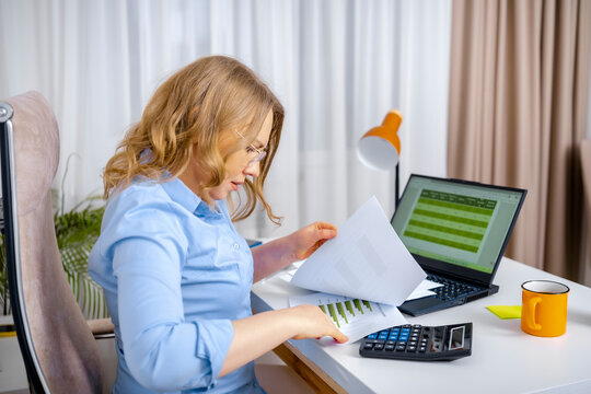 Focused woman working with financial papers, charts, and calculator at office desk. Financial analysis, business accounting concept, budget audit.