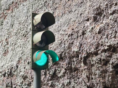 Sem&aacute;foro urbano con luz verde encendida y visera da&ntilde;ada sobre fondo de pared de piedra rugosa