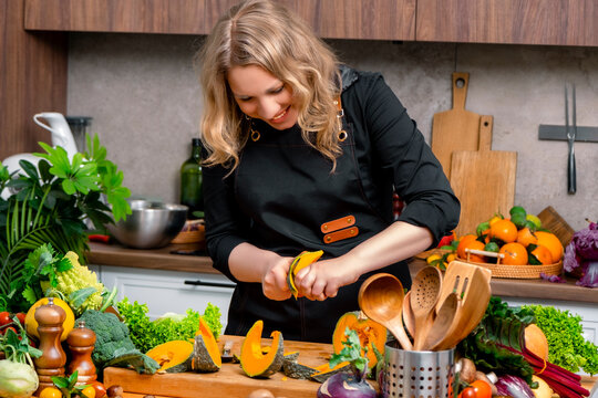 Woman chef peeling ripe pumpkin slice on wooden board in kitchen. Autumn home cooking, seasonal vegetable prep, healthy food recipe, organic autumn comfort food.