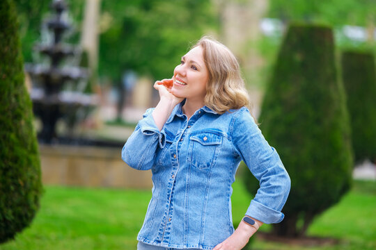 Happy blonde woman posing in green park outdoors. Concept of urban recreation, lifestyle and optimism.