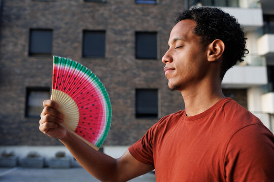 A man using a fan with watermelon design to cool down during a heatwave in the city