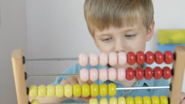 Boy counts colorful beads on wooden abacus while studying at home. Developing mathematical thinking, attention, memory and independent learning through educational play concept. 