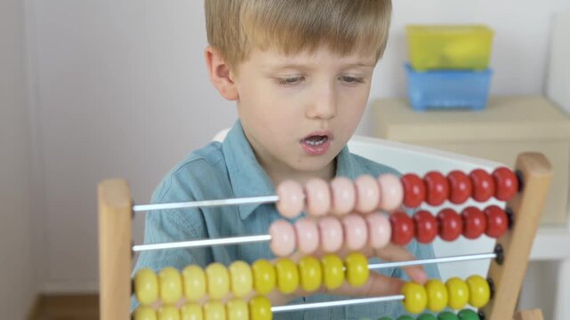 Boy sits at home table with colorful wooden abacus in bright room showing early math learning space. Preschool counting skill and home education concept. 
