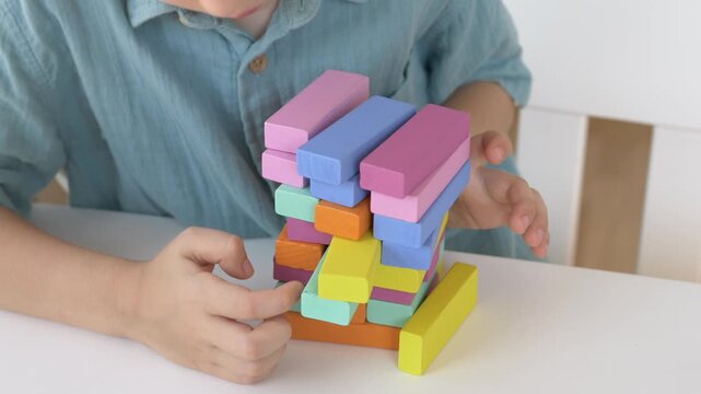 Boy builds colorful wooden Montessori block structure at home table exploring shapes sizes and spatial relationships. Hands on learning and early math concept through natural material play. 