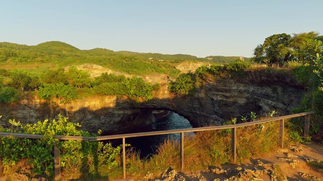 Panoramic View of Natural Coastal Rock Arch and Green Hills Above Ocean at Broken Beach During Golden Hour