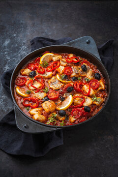Slow cooked fish stew with tomato souce, vegetable and olives served as close-up in a cast iron casserole
