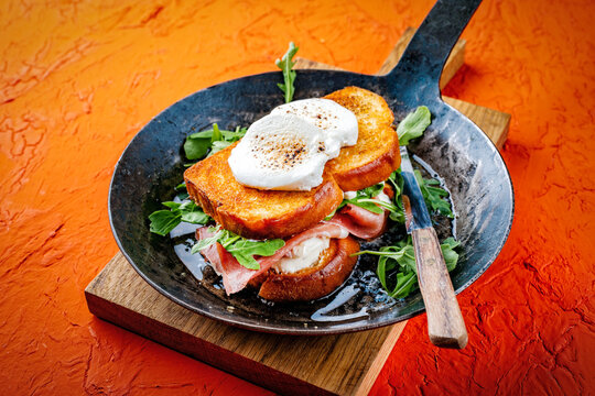 Traditional artisan croque monsieur chevre - hot brioche bread sandwich with prosciutto, arugula and goat cheese roasted in butter served as close-up in a frying pan