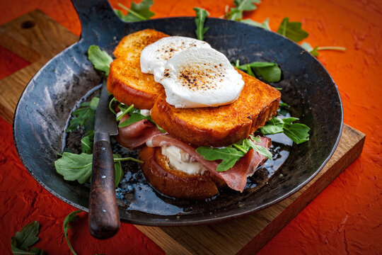 Traditional artisan croque monsieur chevre - hot brioche bread sandwich with prosciutto, arugula and goat cheese roasted in butter served as close-up in a rustic pan