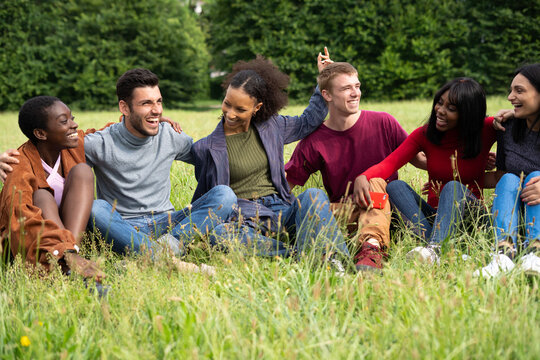 Multiracial Friends Sitting in Grass Field Laughing Together