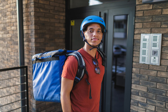 Delivery person with helmet and backpack stands outside of building entrance in the city