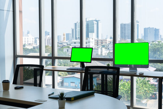 empty co-working space Modern office workspace with office chairs, and two computers with blank white screens for mockup, set against big glass windows overlooking a blurred cityscape.
