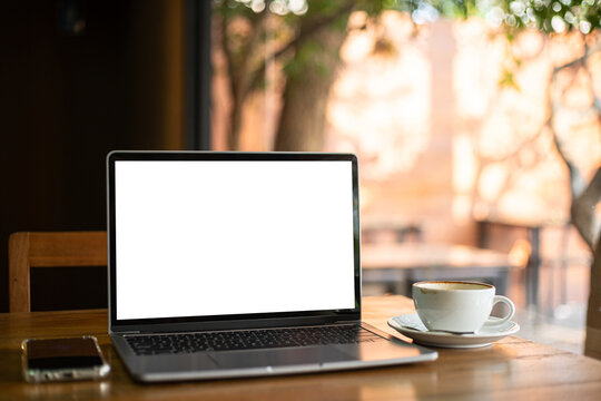 Mockup of laptop computer with empty screen with coffee cup and smartphone on table of tree branch shadow the cafe coffee shop background,White screen