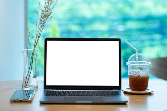 Mockup of laptop computer with empty screen with coffee and smartphone isolate on wooden office desk in coffee shop like the background ,White screen