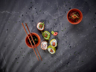 Top view of gourmet sushi rolls on dark stone background with chopsticks and dipping sauces © PERLA