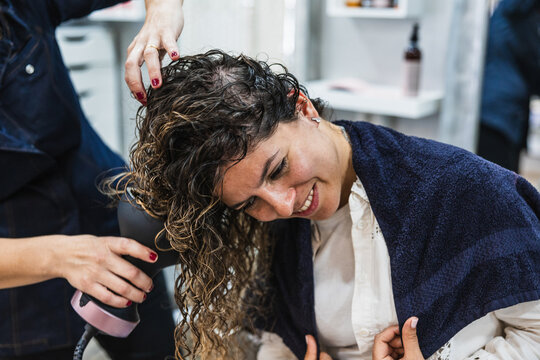 Hairdresser styling woman's curly hair with diffuser