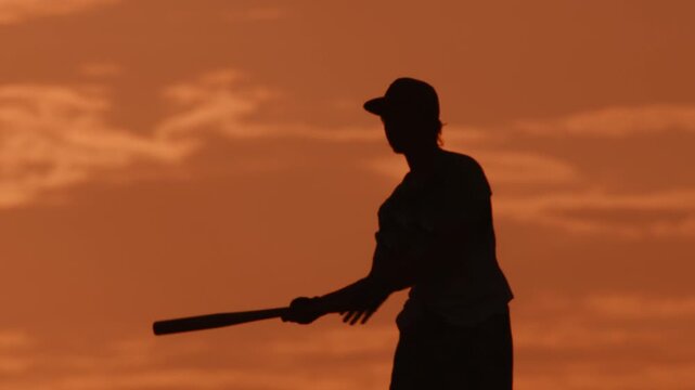 Playing baseball at sunset in an open field with a clear sky and a player holding a bat