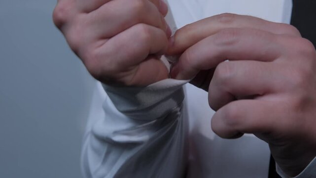 A man in a white shirt fastening a button on his wrist, close-up, white background