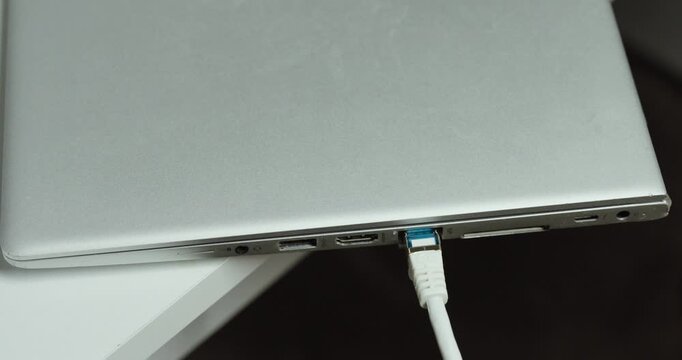 A close-up of a person plugging an Ethernet cable into a laptop and unplugging it again to establish and disconnect a wired network connection.