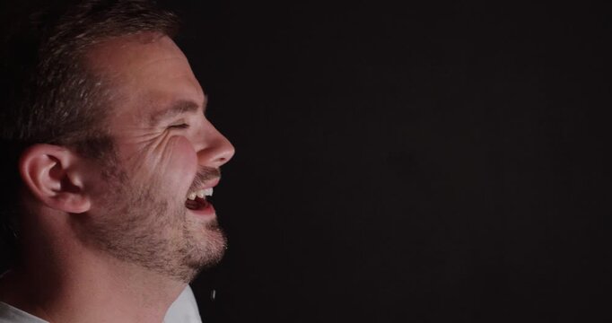 A man bursts into laughter and accidentally spits out water in slow motion, creating a dramatic spray effect against a dark background.