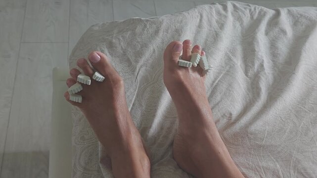 Female feet with toe separators wiggling on a bed. Woman enjoying a relaxing pedicure and foot care treatment for beauty at home or spa