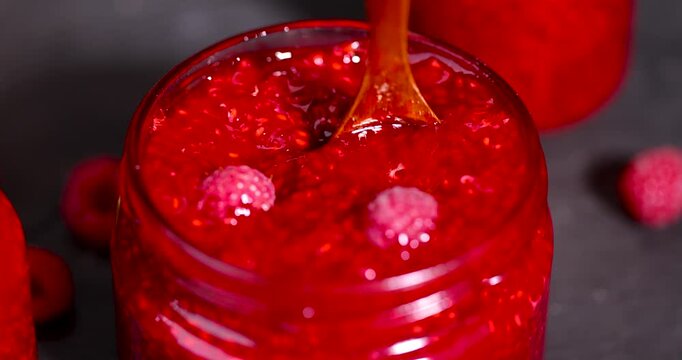 Red homemade grated raspberries in a transparent container, sweet grated raspberries mixed with sugar and placed on a dark slate board with berries